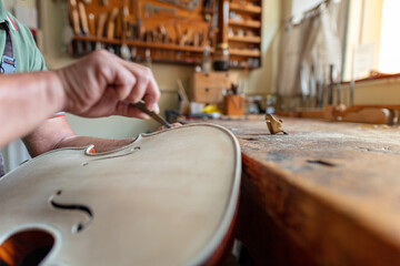 luthier carving the shape of the outside of the front of a violin with gouge