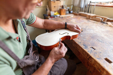 luthier carving the shape of the outside of the front of a violin with gouge