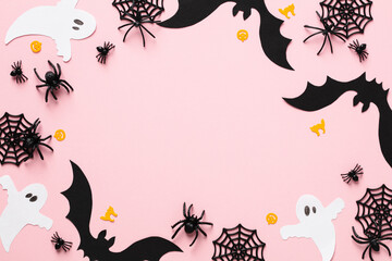 Happy Halloween greeting card design. Frame made of bats, ghosts, spiders, webs on pastel pink background. Flat lay, top view, copy space.