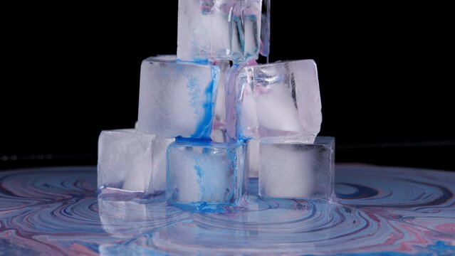 Colored paint spreads over the surface of the ice cubes and flows down onto the plane.