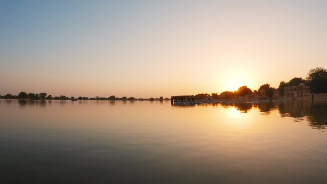 View of the Gadisar Lake during sunset with chhatri in the middle of the lake at Jaisalmer in Rajasthan, India. Reflection of the Chhatri pavilion in the orange water of the lake during sunset.	