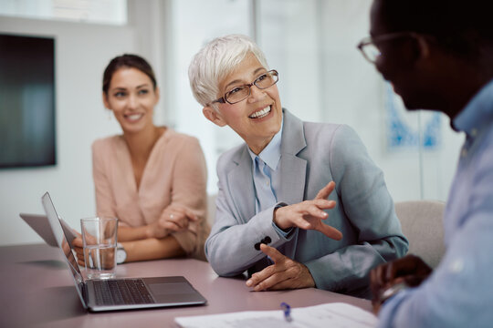 Happy Senior CEO Using Laptop During Meeting With Coworkers In Office.