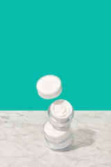 Balancing jars with cosmetic cream on turquoise background