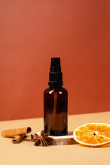 Amber glass cosmetic bottle on wooden podium with cinnamon sticks and slice of orange. Natural beauty product design, branding.