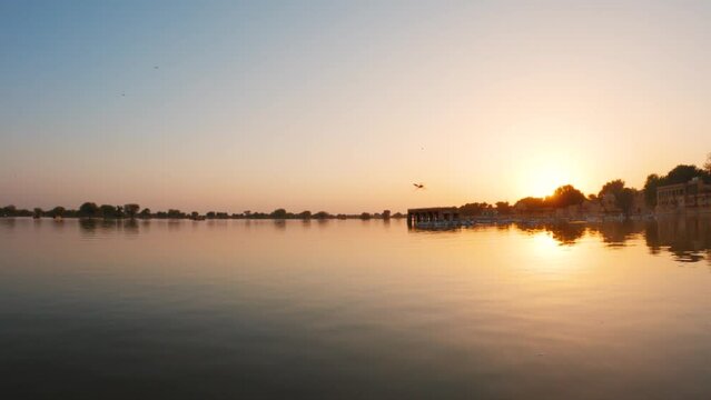 4K View of the Gadisar Lake during sunset with chhatri in the middle of the lake at Jaisalmer in Rajasthan, India. Reflection of the Chhatri pavilion in the orange water of the lake during sunset.	