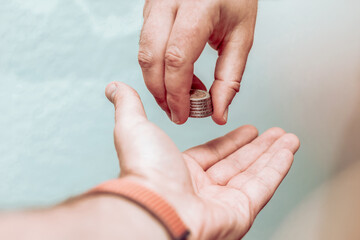 Close up of male hand putting coin into another hand, donation.