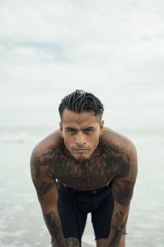 Handsome tanned tattooed sexy man with a naked torso in a flying poreo on the ocean at sunset.
