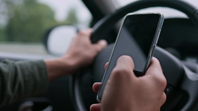 The driver is driving a car holding the steering wheel with a phone in his hands. Driver driving a car holding a phone Driving car with security violations, Hand holding a steering wheel driving a car