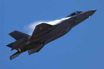 Fototapeta na wymiar Very unusual close view of a F-35A Lightning II in a high G maneuver , with condensation clouds around the plane and afterburner on