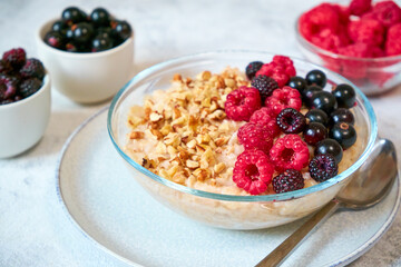 Close-up oatmeal with different berries and crushed nuts in a glass bowl. Healthy balanced food