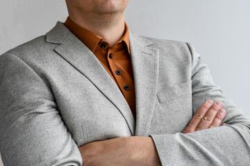 Close up of businessman with arms crossed wearing white tweed jacket with beige polo.