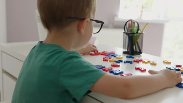 back view baby kid boy in glasses completing word mama with alphabet letters on white desk. learning at home, early education, abc colorful letters, first words. concept family education children