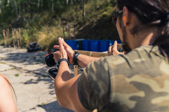 Rear view of white man in camo t-shirt practising how to aim handgun. Firearm training at firing range. Outdoor horizontal shot. High quality photo