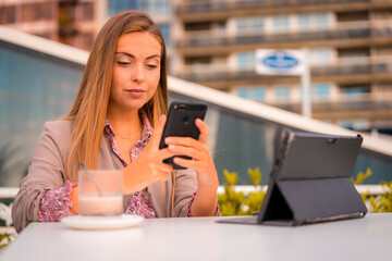 Executive blonde woman, businesswoman having a coffee decaffeinated breakfast writing a message with the phone