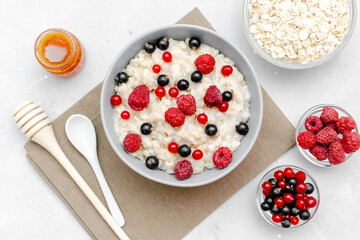 Oatmeal porridge with summer raspberry, currant berries,honey. Porridge oats in bowl with fruits. Healthy food breakfast,lifestyle,dieting, proper nutrition.Top view flat lay on gray table background
