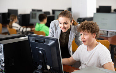 Fototapeta premium Smiling friendly female teacher talking to cheerful teenager studying in college computer lab..