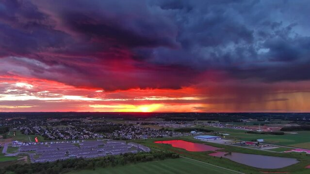 Exceptionally beautiful red sunset with rain clouds over rural suburb at dusk, aerial view.
