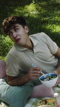 a young white man enjoying a salad in the park