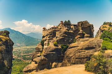 Impressive orthodox mountain monasteries. Beautiful view of one side of Meteora Monastery built on high rock formation. Blue sky. Greek city in the background. High quality photo