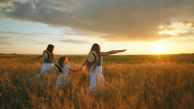 happy little sisters are walking in golden farmland in harvesting season, admiring sunset in fields