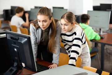Positive woman teacher together with the girl teaches how to work on the computer