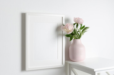 Frame mockup on white wall with peony flowers in vase, blank mockup for print presentation