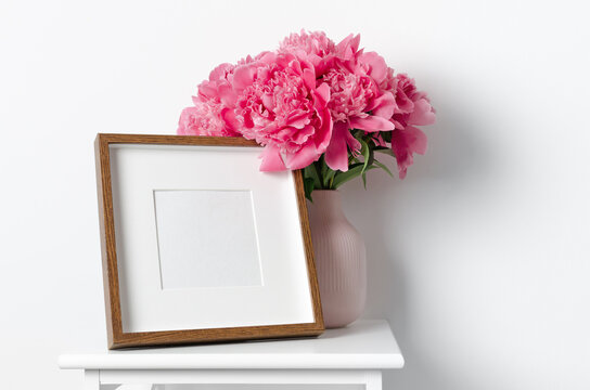 Blank square frame mockup with fresh peony flowers in white room interior