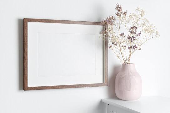 Wooden frame mockup on white wall with dry flowers in vase