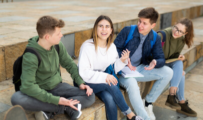Cheerful teenagers sitting together, talking and having fun outdoors