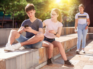 Focused teenager carried away with smartphone not paying attention to his girlfriend outdoor on summer day