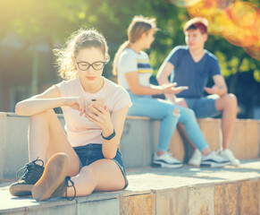Teen girl is passionate about playing on smartphone while friends are sitting nearby