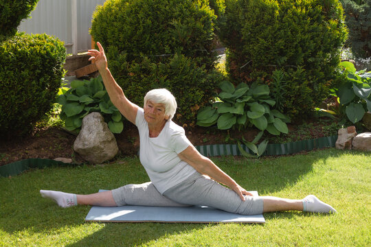 an aged elderly gray-haired woman does therapeutic exercises for stretching muscles and hip joints. exercise splits, yoga asana. High quality photo