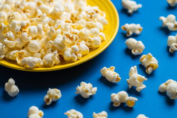Popcorn on a yellow plate on blue background, Food or snack, Health or salt