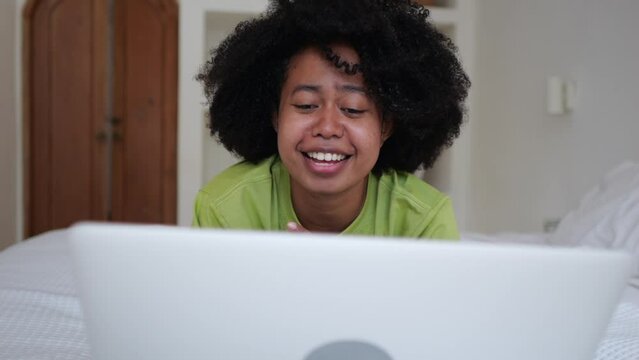 Multicultural woman on bed chatting cutely with her husband via video call on laptop from her bedroom. A black woman with an afra hairstyle is happy that she can communicate with her husband online.