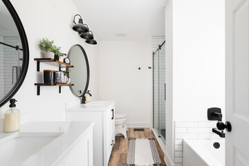 A modern farmhouse bathroom with a white vanity and marble countertop, circular black mirrors, and a view to the white subway tile shower. - obrazy, fototapety, plakaty