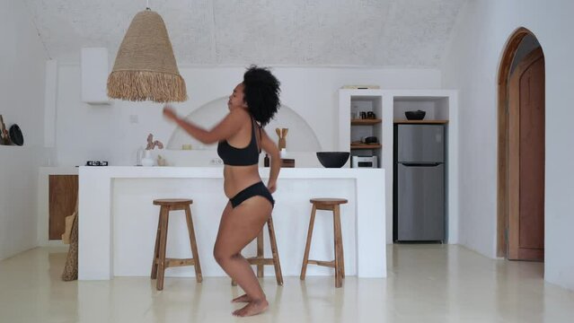 African American model plus size dancing at home in the kitchen in black lingerie. The woman does not pay attention to excess weight. An overweight woman loves and accepts herself.