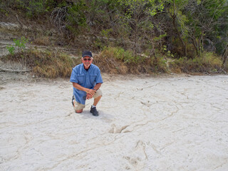 Senior man kneeling next to dinosaur footprint