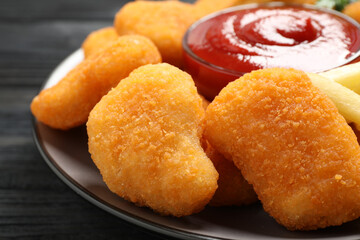 Tasty fried chicken nuggets served on black wooden table, closeup