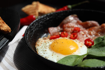 Tasty fried egg with bacon, chili pepper and spinach on table, closeup