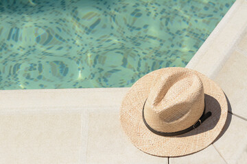 Fototapeta na wymiar Stylish hat near outdoor swimming pool on sunny day, space for text. Beach accessory