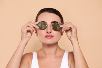 Beautiful woman applying green tea bags on skin under eyes against beige background