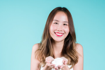 Happy charming young Asian woman applying facial foam cleanser wash and scrub on her face on the blue background.