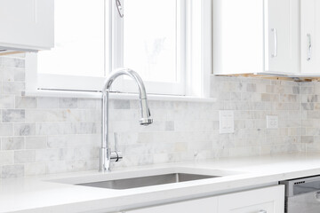 A kitchen sink detail shot with white cabinets and a marble subway tile backsplash.