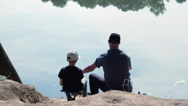 Father and son sitting together,bonding freshwater fishing a lake in Bulgaria shot from behind hand held