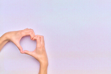 woman's hands making a heart gesture in the corner of the image with a bright white background