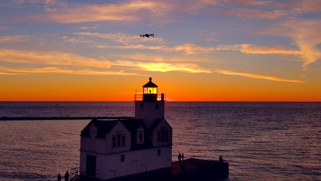 Incredible sunrise sky over lighthouse, drones flying and filming. Silhouetted people fishing.
