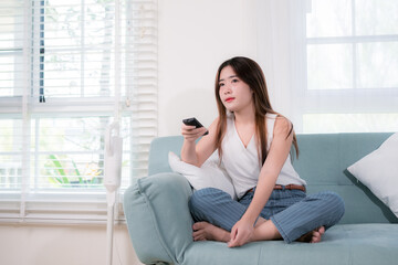 Asian woman use remote control for watching tv her bored unhappy emotion sitting near sofa in living room at home
