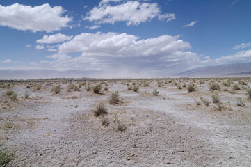 Death Valley desert floor showing a sand storm in the backgrond. Windy day with blue sky and clouds.
