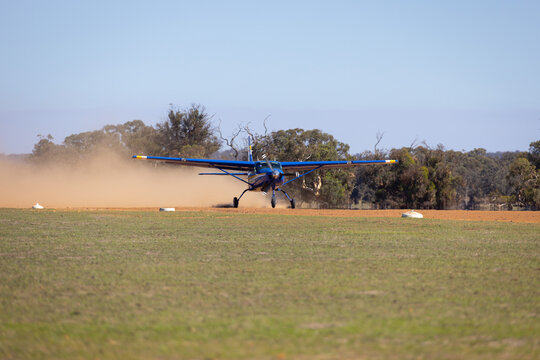 small plane taxiing on unsealed dusty runway in rural area
