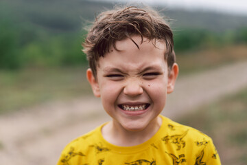 A six year old boy smiles at the camera in the park. Happy child boy laughing and playing in the summer day